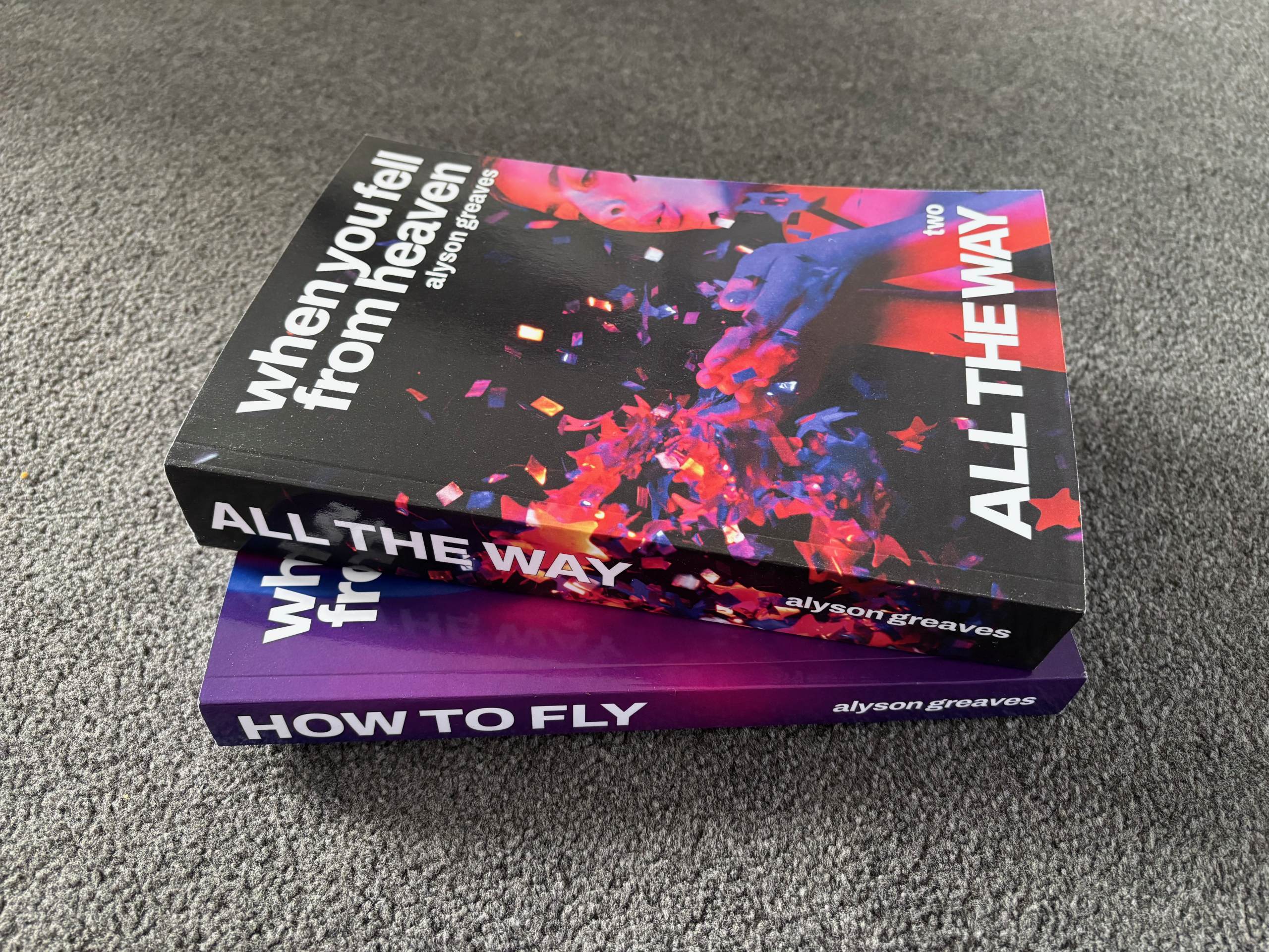 A Physical Copy of "All the Way" by Alyson Greaves on top of a physical copy of "How to Fly" by the same author.